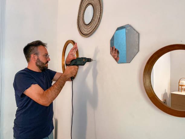 Man drilling the wall with a drill to hang a mirror