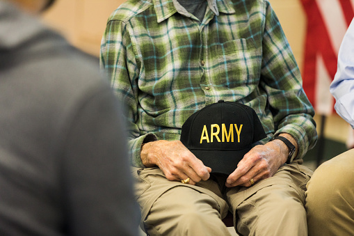 A low angle view of an unrecognizable senior adult male veteran holding an army cap in his lap as he attends the therapy group meeting.