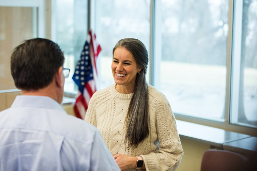An unrecognizable mature adult male veteran talks with the mature adult female therapist before the support group meeting in the community center.