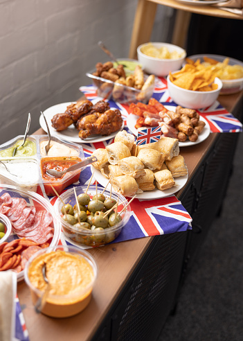 A shot of a table covered in homemade snacks in an office workplace in the North East of England, bunting Union Jack flags are hanging around the room and the snacks are ready to eat.