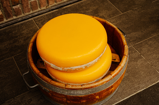 Two whole Gouda cheese rounds in a bowl on a wooden bench in Volendam, North Holland.