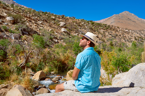 Caucasian mid-adult male sitting on a rock relaxingly contemplating the landscape of the Cochiguaz Valley Paihuano