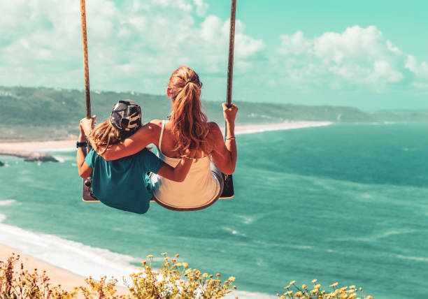Mother and son having fun on swing above atlantic ocean- Portugal, Nazare- family love, vacation, relaxing, tourism,tropical beach concept stock photo