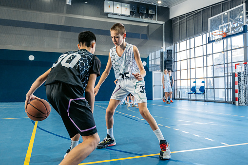 Group of male teenagers playing basketball in an indoor court.