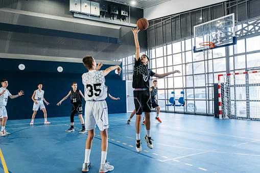 Group of male teenagers playing basketball in an indoor court.