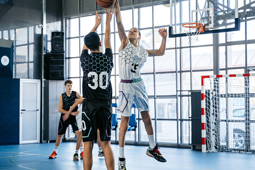 Group of male teenagers playing basketball in an indoor court.