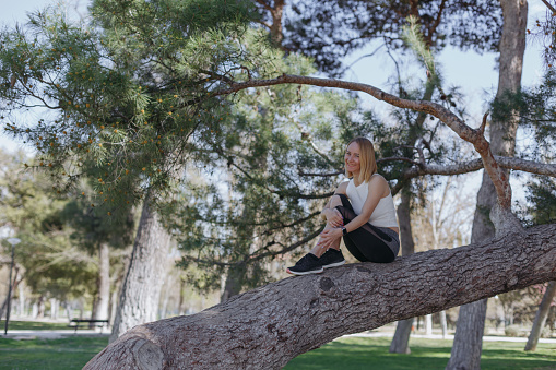 Молодая женщина сидит на дереве в парке