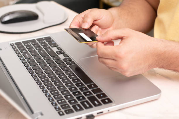 person holding a credit card with two hands front a laptop, e-comerce and online shopping concept - comerce imagens e fotografias de stock