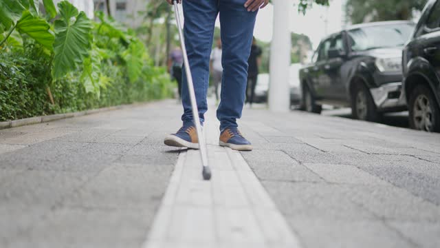 Low section of a blind man walking in the street with his walking cane