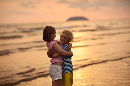 Child playing on ocean beach. Kid jumping in the waves at sunset. Sea vacation for family. Little boy and girl running on exotic island on summer holiday. Friendship and love. Siblings hug, hold hands