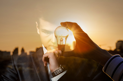 The concept of brainstorming and emerging ideas. Double exposure of a thinking businessman and burning light bulbs against the backdrop of the sun.