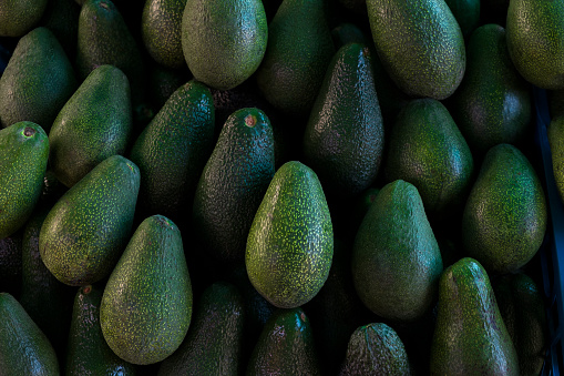 Clean eating concept. Bunch of ripe freshly picked avocados at local produce farmers market stand. Close up, background, copy space.