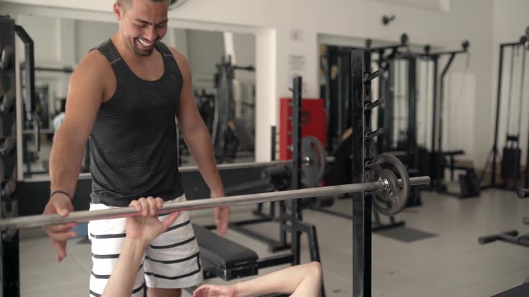 Smiling gym instructor helping a man workout with barbells