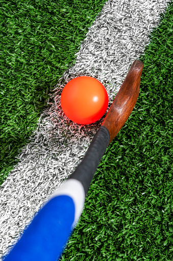 Looking down on a wooden field hockey stick with an orange ball sitting on the center line