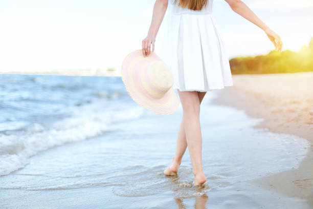 istock Young woman on a beach holding a white hat. Legs close up 1487362412