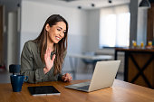Satisfied female entrepreneur waving hand looking at laptop during virtual video conference call in home office