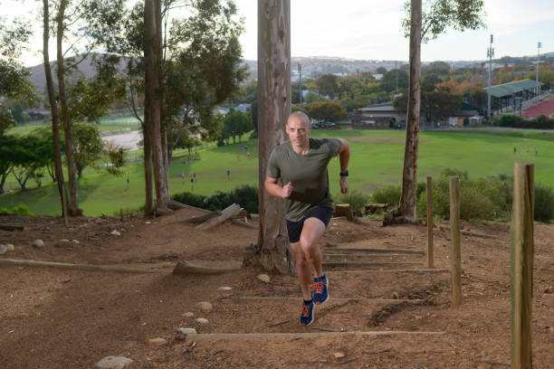 completely bald male exercising running steps doing strength exercises in a forest above a sports field - completely bald imagens e fotografias de stock