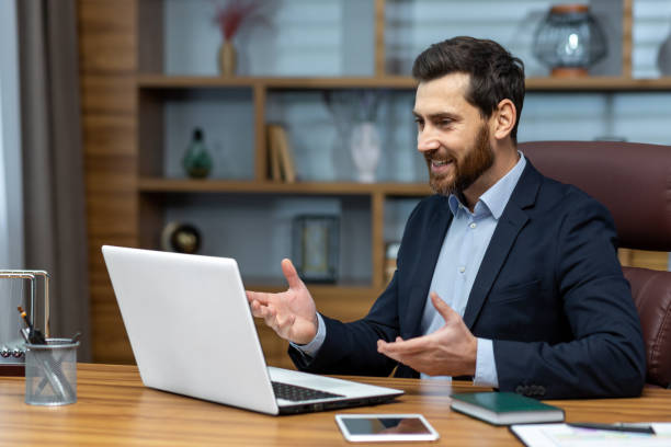 istock Successful smiling boss talking on video call, man in business suit inside office using laptop for online meeting, businessman joyfully talking and reporting 1487363812