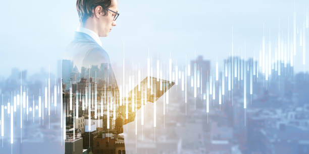 istock Attractive young european businessman using pad with glowing candlestick forex chart on blurry light city background. Trade, finance and concept. Double exposure. 1487369078