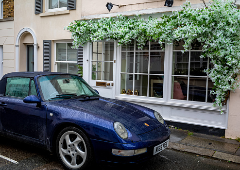View of a sports car parked on a lovely mews street in the exclusive Belgravia section of London, England.  Flowers decorate the window of the mews home opposite the car.