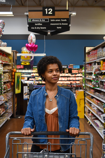 A young African-American woman pushes her shopping cart down the dry goods aisle of a grocery store
