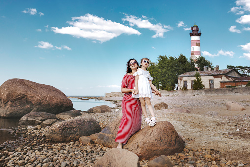 happy little girl of 5 years and her mother on beach next to lighthouse in summer, mother's day