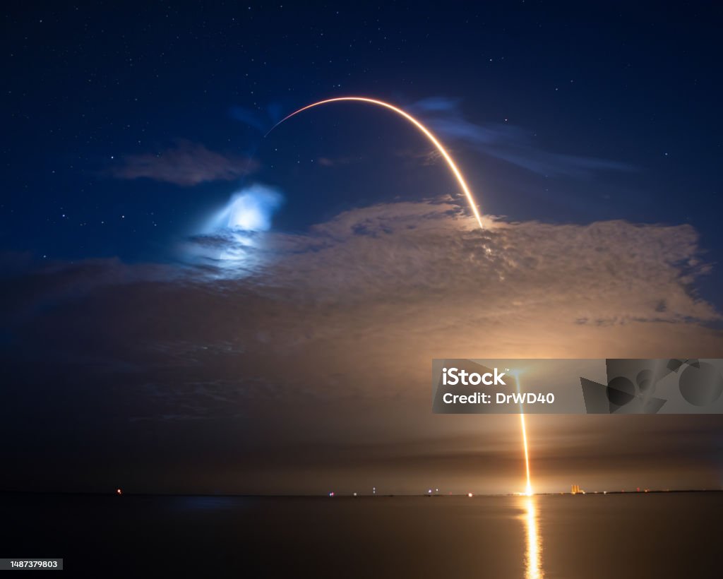 A Rocket Launch Streaks into a Florida Starry Night Cosmic Voyage: A Rocket Streaking Across the Star-Studded Night Sky in Florida piercing a cloud Space Exploration Stock Photo