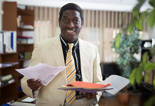 Portrait of a positive african american businessman in the office, holding important documents for work