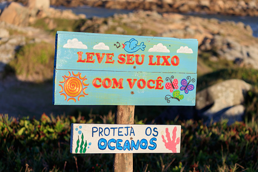 Description: This vibrant sign, written in Portuguese, reminds beach-goers to be mindful of their impact on the ocean by encouraging them to take their trash with them. Its bright colors and bold lettering make it hard to miss, and its message is an important one for preserving the natural beauty of the coastline. Located on the stunning Praia da Vila in Imbituba, SC, this sign serves as a reminder to tourists and locals alike to do their part in protecting the oceans.