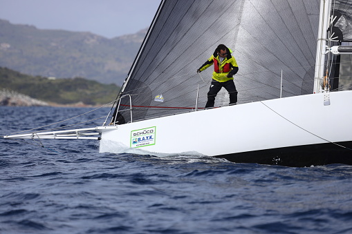 Bodrum,Mugla, Turkey. April 01, 2023: sailor team driving sail boat in motion, sailboat wheeling with water splashes, mountains and seascape on background. Sailboats sail in windy weather in the blue waters of the Aegean Sea, on the shores of the famous holiday destination Bodrum