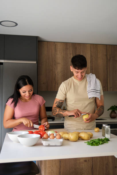 istock Two young latin people peeling potatoes and cutting tomatoes at kitchen. 1487391159