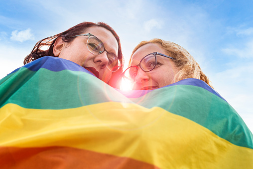 Lesbian couple under LGBT rainbow flag while looking at camera. Concept of Pride. Pride month.