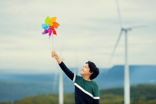 niño asiático progresivo jugando con un juguete de molinete de viento en una granja de turbinas eólicas. - run of the mill fotografías e imágenes de stock