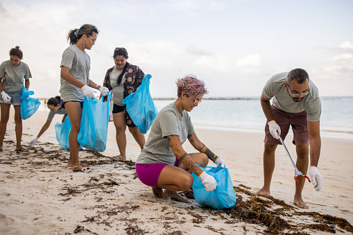 Multiracial group of people, male and female volunteers cleaning the beach together.