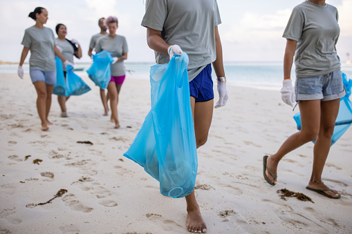 Multiracial group of people, male and female volunteer activists carrying garbage bags after cleaning the beach together.