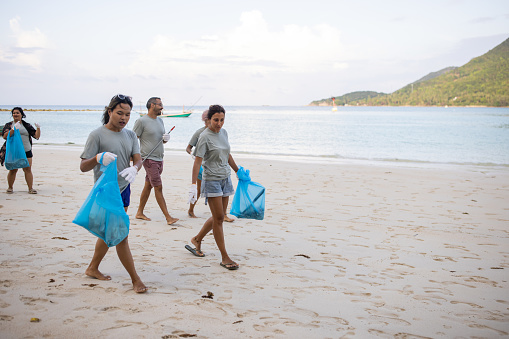 Multiracial group of people, male and female volunteer activists carrying garbage bags after cleaning the beach together.
