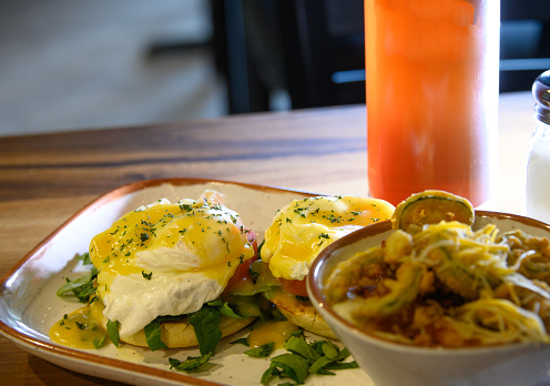 A fresh plate of eggs Benedict with a side of friend vegetables.