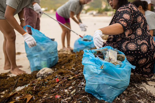 Multiracial group of people, male and female volunteers making an effort cleaning the beach together.