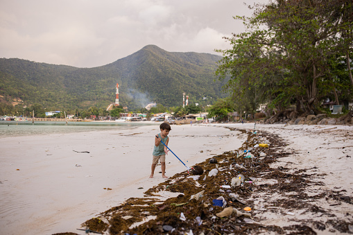Little boy volunteer activist picking up garbage with mechanical grabber from the beach.