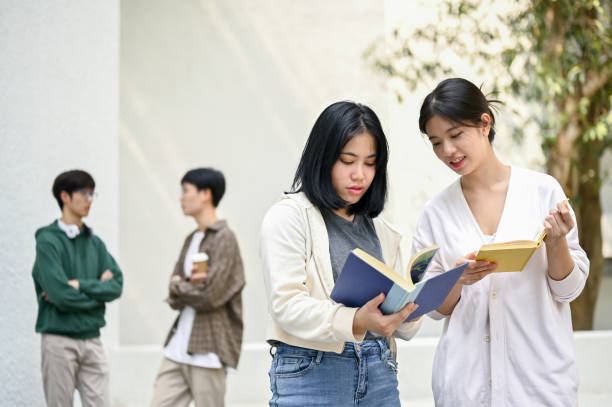istock Two charming Asian female college students are discussing and searching informations in a book 1487413996