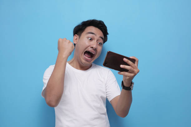 istock Funny Young Asian Guy Playing Games on Tablet 1487414019