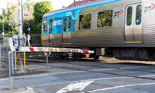 Brunswick, Victoria, Australia, April 13, 2023: A Metro train passes as the boom gate is in position at the level crossing near Brunswick station