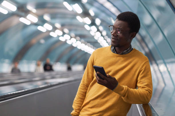 istock Young businessman with smartphone standing on escalator 1487423693