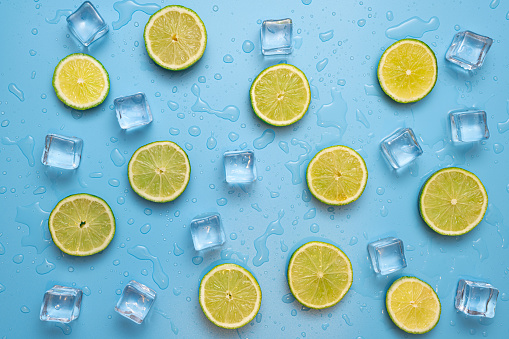 Concept for fresh, fruity and juicy fruit. Top view. Delicious fruit background made of fresh sliced lemon and lime fruits on a blue background with ice cubes and waterdrops