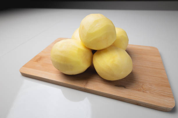 pile of peeled potatoes on a wooden cutting board. Clean potatoes on the table. Cook food, peel potatoes stock photo
