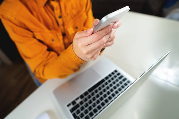 istock Woman's hand with a mobile phone over a laptop, top view. Workplace at home, freelancer 1487429681