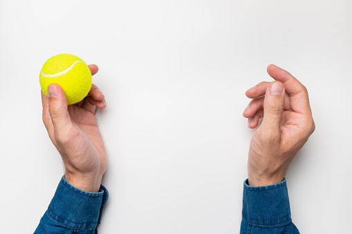 The man throws the ball from hand to hand. Hands and green-yellow tennis ball top view on white background.