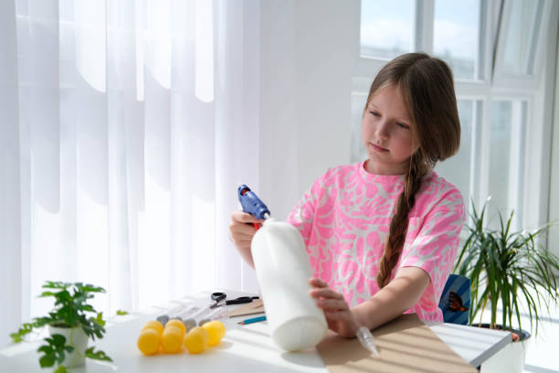 istock Step-by-step instructions for making crafts from improvised materials. Handmade at school craft rocket for the day of cosmonautics. The child is gluing parts to a plastic bottle.  Step 1 1487430858