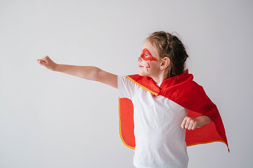 Funny little super hero girl in a red cloak. Superhero concept. Little child playing hero in the kids