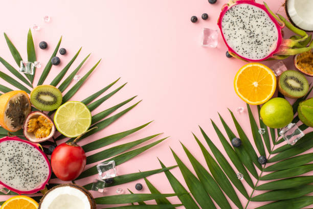 Refreshing summer treats. A top view flat lay of exotic fruits like dragon fruit, kiwi, orange, lime, and coconut, tomarillo with palm leaves on a pink backdrop advertising copy